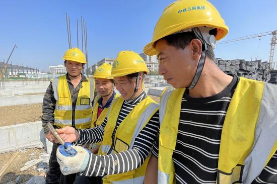 路桥公司安徽新桥产业园项目劳务工在现场利用工休时间通过手机收看开幕会直播。 韩宇恒摄